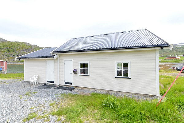 Gemütliches Ferienhaus in Nord-Norwegen, umgeben von grüner Landschaft; ideal für Angelurlaub. Das weiße Gebäude mit schwarzem Dach bietet Ruhe und Nähe zur Natur. Perfekt für Erholung und Abenteuer in skandinavischer Idylle.