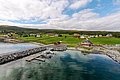 Luftaufnahme eines norwegischen Küstendorfs in Nord-Norwegen, mit malerischen bunten Häusern, grünen Feldern und einem ruhigen Bootsanleger am klaren Fjordwasser. Perfekt für Angelurlaube und Naturerlebnisse.
