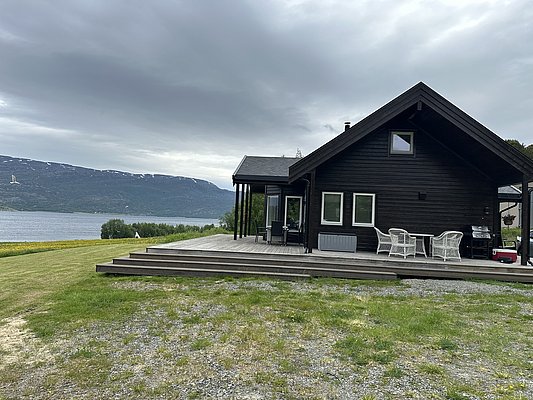Gemütliches Holzhaus am Fjord in Nord-Norwegen, umgeben von Bergen und grüner Wiese. Perfekter Ort für einen entspannten Angelurlaub mit atemberaubender Aussicht und Nähe zur Natur.
