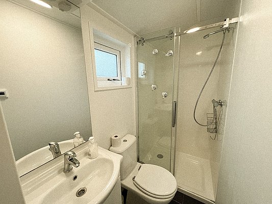 Modernes, helles Badezimmer in Nord-Norwegen: Dusche mit Glastür, Waschbecken, Toilette und Fenster. Funktional und komfortabel, ideal für Angelreisende. Perfekt, um sich nach einem Tag auf See zu entspannen.