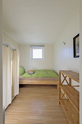 Helles, gemütliches Zimmer in Nordland, Norwegen: Holzboden, grünes Bett, kleines Fenster, offene Regale. Optimal für ruhigen Angelurlaub. Entspannung und Komfort in idyllischer Umgebung erleben. Perfekt für Naturliebhaber und Erholungssuchende.