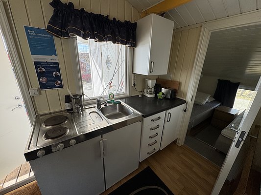 Gemütliche Ferienwohnung in Hitra, Norwegen. Moderne Küche mit Spüle, Herd und Kaffeemaschine. Helles Schlafzimmer im skandinavischen Stil nebenan. Perfekter Rückzugsort für Angler, die in dieser fischreichen Region entspannen möchten.