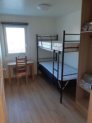Helles, schlichtes Zimmer in Nordland, Norwegen, mit Etagenbett, Holzfußboden und Schreibtisch vor dem Fenster. Perfekt für Angelurlauber, die Komfort und Einfachheit schätzen. Ideal für erholsame Nächte nach spannenden Angelausflügen.