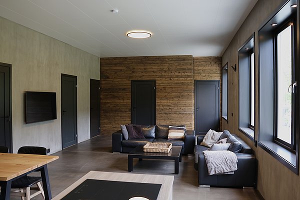 Gemütlicher Wohnbereich in Nordland, Norwegen, mit moderner Inneneinrichtung. Schwarze Ledersofas, Holzelemente und große Fenster schaffen eine warme Atmosphäre. Ideal für entspannte Angelreisen in der beeindruckenden Landschaft.