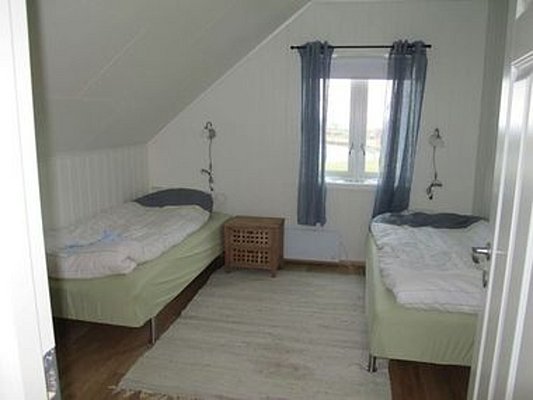 Gemütliches Schlafzimmer in Nord-Norwegen mit zwei Einzelbetten, hellem Holzboden, blauem Vorhang und einem kleinen Fenster. Ideal für Erholung nach einem erlebnisreichen Angeltag. Perfekte Unterkunft für Angelreisen in Norwegen.