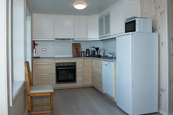 Eine moderne Küche mit hellen Holz- und weißen Schränken, ausgestattet mit einem Herd, Kühlschrank, Mikrowelle und einer Spüle.