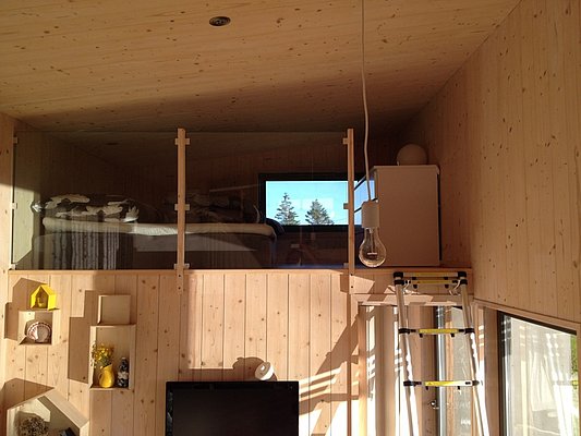Gemütliche Holzkabine in Nordland, Norwegen, mit Schlafbereich im Loft-Stil. Große Fenster bieten Blick auf Natur; ideal für Angelurlaub. Moderne, minimalistische Einrichtung mit hölzernem Interieur. Perfekt für Abenteuer in skandinavischer Wildnis.