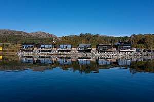 Moderne Ferienhäuser am ruhigen Ufer in Hitra, Norwegen, spiegeln sich im klaren Wasser. Die idyllische Landschaft lädt zu Angelabenteuern und Entspannung ein. Perfekt für Angelurlauber auf der Suche nach Natur und Komfort.