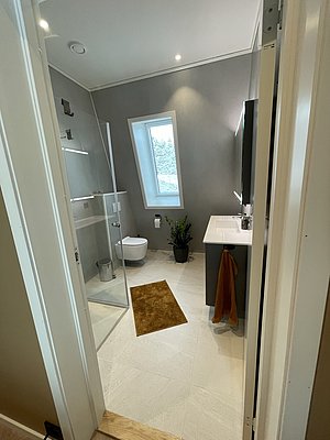 Modernes Badezimmer in Hitra, Norwegen: Elegantes Design mit Glasdusche, weißem Waschtisch, grauen Wänden und Fenster mit Aussicht. Perfekt für entspannte Angelreisen in skandinavischer Umgebung.