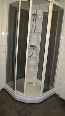 Eckdusche in modernem Badezimmer, gefliest mit grauen und weißen Fliesen, in Hitra, Norwegen. Komfortabler Einstieg mit Glastüren für entspannende Erfrischung nach dem Angeln. Ideal für Angelreisende, die Ruhe und Bequemlichkeit suchen.