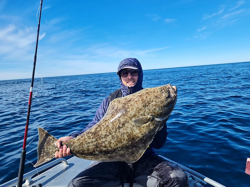 Ein Angler hält stolz einen großen Fisch auf einem Boot im sonnenbeschienenen River Shannon, Irland. Blauer Himmel und klares Wasser bieten perfekte Bedingungen für Angelreisen. Ideal für Abenteuerlustige und Erholungssuchende.