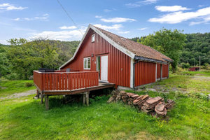 Rotes Holzhaus in Süd-Norwegen, umgeben von grüner Landschaft und Wald. Gemütliche Terrasse ideal für Angelabenteuer und Naturerlebnisse. Perfekt für Erholung und Entspannung in skandinavischer Idylle. Perfekt für deinen nächsten Angelurlaub.