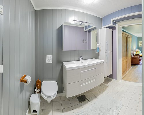 Modernes Badezimmer in Nordland, Norwegen: Graue Holzverkleidung, weiße Einrichtung, große Spiegel, dezente Beleuchtung, direkter Zugang zum Wohnbereich. Perfekt für Angelurlauber, die Komfort nach einem Tag am Fjord suchen.
