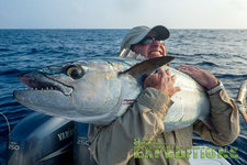 Ein Angler in Tansania hält einen großen Thunfisch stolz über der Schulter. Im Hintergrund das weite Meer und ein Bootsmotor. Perfekter Angelmoment für Abenteurer.