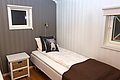 Gemütliches Schlafzimmer in Nord-Norwegen mit Einzelbett, brauner Decke und Kissen mit Tiermotiv. Weiße Holzwände und Fenster sorgen für eine helle, freundliche Atmosphäre. Perfekt für erholsame Angelurlaube in Skandinavien.