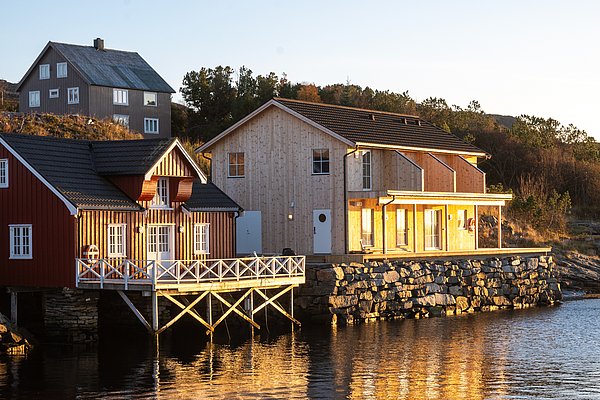 Gemütliche Holzcottages am Wasser in Hitra, Norwegen, in warmem Sonnenlicht. Perfekt für Angelurlaube und Naturerlebnisse in malerischer Umgebung. Entdecke die Ruhe und Schönheit der skandinavischen Küstenlandschaft.