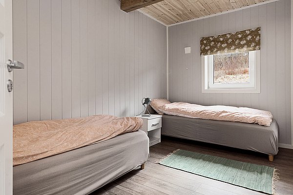 Gemütliches Schlafzimmer in Nordland, Norwegen, mit zwei Einzelbetten, Holzwänden und Fenster. Ideal für Angelurlauber. Natürliche Einrichtung sorgt für Entspannung nach einem abenteuerlichen Tag beim Angeln.