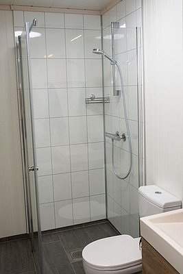 Modernes Badezimmer in Nord-Norwegen mit weiß gefliester Dusche, Glaswand und eleganter Ausstattung. Perfekt für gemütliche Angelurlaube und Entspannung nach einem erfolgreichen Tag am Wasser. Optimal für Komfort und Erholung.