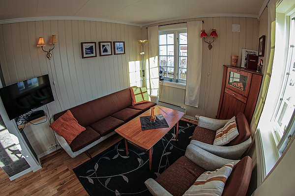 Gemütliches Wohnzimmer in Nord-Norwegen mit Holzmöbeln, bequemen Sesseln, Sofa, Flachbildfernseher und großen Fenstern. Ideal für entspannte Abende nach einem erlebnisreichen Angelurlaub. Helle, einladende Atmosphäre mit dekorativen Elementen.