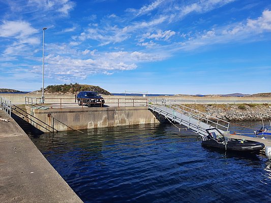 Klare blaugrüne Küstengewässer in Hitra, Norwegen, ideales Angelrevier. Ein ruhiger Hafen mit Bootsanleger vor malerischer Landschaft, perfekt für Meeresangeln und Erholung in naturnaher Umgebung. Perfekte Destination für abenteuerliche Angelreisen.