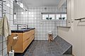 Modernes Badezimmer in Nord-Norwegen mit großem Spiegel, Holzkommode und eleganten Fliesen. Helle Beleuchtung, Fenster mit Pflanzen, und ein Hocker mit Handtüchern sorgen für Komfort und Stil. Ideal für erholsamen Angelurlaub.