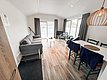 Eine gemütliche skandinavische Ferienwohnung in Nord-Norwegen mit Blick auf das Wasser. Helle Einrichtung, Holzfußboden, graues Sofa und Esstisch für einladende Angelurlaube in idyllischer Umgebung. Ideal für erholsames Wohnen nach einem Angelausflug.