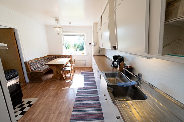 Gemütliche nordische Küche in Nordland, Norwegen, mit Holzmöbeln und großem Fenster. Ideal für Angelurlaub, kombiniert traditionelle Elemente mit moderner Funktionalität. Sonnendurchfluteter Raum, perfekter Ausblick auf umliegende Natur.