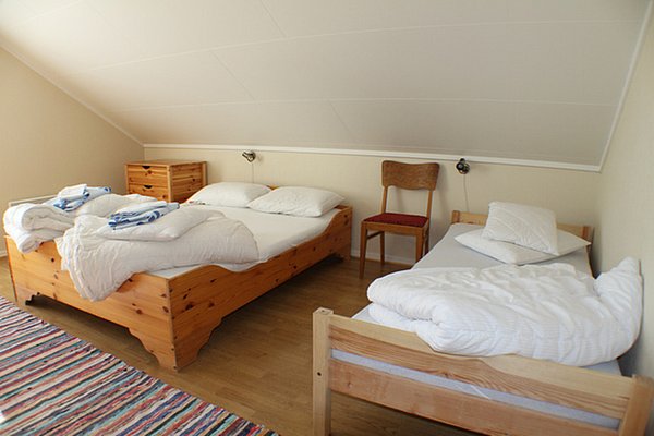 Gemütliches Schlafzimmer in Hitra, Norwegen: Drei hölzerne Einzelbetten mit weißer Bettwäsche und blauen Handtüchern, Holzboden, kleine Kommode. Ideal für entspannten Angelurlaub.
