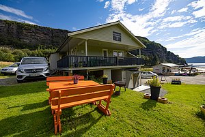 Frühstücksterrasse mit Blick auf ein modernes Ferienhaus in Hitra, Norwegen. Im Hintergrund malerische Küstenlandschaft und zahlreiche Boote. Perfekter Ausgangspunkt für Angelabenteuer und Naturerlebnisse in eindrucksvoller Umgebung.
