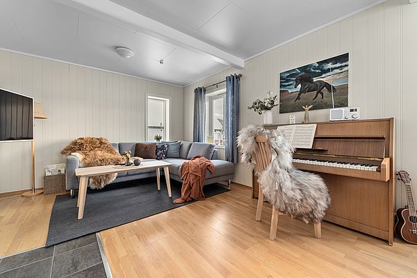 Gemütliches skandinavisches Wohnzimmer in Nord-Norwegen mit grauem Sofa, Holzmöbeln, Klavier, und Dekorfellen. Warme, einladende Atmosphäre, ideal für Entspannung nach einem Angelabenteuer. Perfekter Ort, um die Schönheit Nordnorwegens zu genießen.