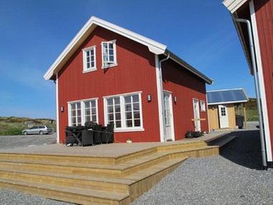 Rotes, skandinavisches Ferienhaus in Nordland, Norwegen, bei klarem blauen Himmel. Ideal für Angelreisen bietet die Unterkunft Komfort und Gemütlichkeit. Perfekte Basis für Abenteuer in beeindruckender Naturkulisse.