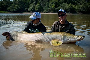 Zwei Angler im Wasser halten einen beeindruckend großen Fisch, umgeben von traumhafter norwegischer Landschaft bei Hitra. Perfektes Angelabenteuer mit Andree's Angelreisen, voller Spannung und großartigen Fangchancen.