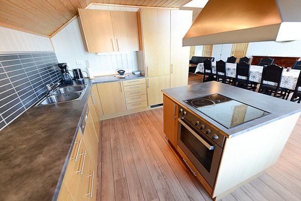 Moderne Küche in Nordland, Norwegen, mit Holzschränken, Kochinsel und Essbereich. Ideal für Angelreisende, die Komfort und Funktionalität in ihrem Ferienhaus suchen. Perfekter Ausgangspunkt für ein unvergessliches Angelabenteuer.