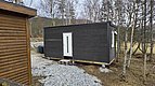 Kleine, moderne Holzhütte in Nordland, Norwegen, umgeben von lichten Bäumen und Schotterweg. Ideal für Angelurlaub und Naturerlebnis. Ruhige, abgelegene Lage in der skandinavischen Wildnis.
