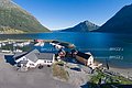 Luftaufnahme der Nordland-Küste in Norwegen mit malerischer Hafenanlage, umgeben von majestätischen Bergen und klarem Wasser. Drei Brygges (Anlegestellen) laden zum Angeln und Entdecken ein. Ideal für Angelurlauber und Naturfreunde.