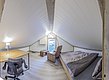 Gemütliches Dachgeschosszimmer in Nordland, Norwegen, mit Holzboden, Doppelbett, Schreibtisch und Sessel. Ideal für Angelurlaub, bietet es Entspannung nach einem erfolgreichen Angelausflug. Helle, freundliche Atmosphäre mit kleinem Fensterblick ins Grüne.