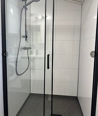 Moderne, geräumige Duschkabine mit Glaswänden und schwarzem Rahmen in einem Badezimmer auf Hitra, Norwegen. Ideal für Erholung nach einem langen Angeltag. Sauberes, minimalistisches Design unterstreicht Wohlfühlambiente im Angelurlaub.