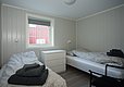 Gemütliches Schlafzimmer in Hitra, Norwegen mit zwei Einzelbetten, schlichter Einrichtung und hellen Wänden. Perfekte Unterkunft für Angelreisen, bietet Entspannung nach einem erlebnisreichen Tag. Fenster mit Ausblick auf rotes Holzhaus.