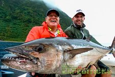 Zwei Angler in Tanzania präsentieren stolz ihren beeindruckenden Fang: einen großen, glänzenden Fisch. Die üppige grüne Landschaft im Hintergrund unterstreicht das Abenteuer im exotischen Angelurlaub.
