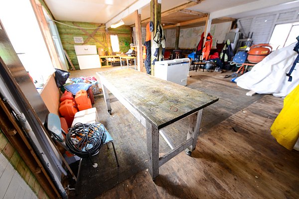 Eine rustikale, hölzerne Fischerhütte in Nord-Norwegen mit Arbeitsbereich, Fischeranzügen und Ausrüstung, ideal für Vorbereitungen auf ein erfolgreiches Seeabenteuer. Perfekt für Angelreisen und Entdecker im hohen Norden.