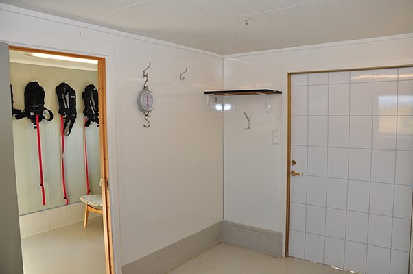 Heller, praktischer Trockenraum in Nord-Norwegen mit Haken, Waage und Stauraum, ideal für Angelurlaub. Im Nebenraum hängen Schwimmwesten – perfekt zur Vorbereitung auf Meeresabenteuer.