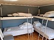 Ein Schlafraum mit vier weißen Etagenbetten und blauer Wand, ausgestattet mit Leitern und Decken auf Holzboden.