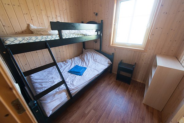 Gemütliches Schlafzimmer mit Hochbett in Nordland, Norwegen. Holzverkleidung, Tageslichtfenster und schlichte Möbel schaffen eine einladende Atmosphäre. Ideal für deinen Angelurlaub in Skandinavien.