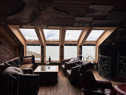 Gemütliches Wohnzimmer in Nord-Norwegen mit Ledermöbeln, Holzboden und großer Fensterfront mit Meeresblick. Ideal für Angelreisen und Entspannung in malerischer Naturkulisse. Perfekt für Abenteuerlustige und Erholungssuchende.