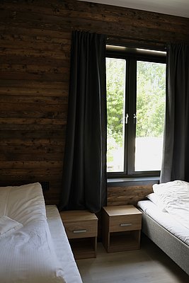 Gemütliches Schlafzimmer in Nordland, Norwegen: Hölzerne Wände, zwei Einzelbetten mit Nachttischen, Fensterblick auf grünes Laub. Ideal für erholsame Angelreisen und Entdeckungen in Skandinavien.