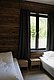 Gemütliches Schlafzimmer in Nordland, Norwegen: Hölzerne Wände, zwei Einzelbetten mit Nachttischen, Fensterblick auf grünes Laub. Ideal für erholsame Angelreisen und Entdeckungen in Skandinavien.