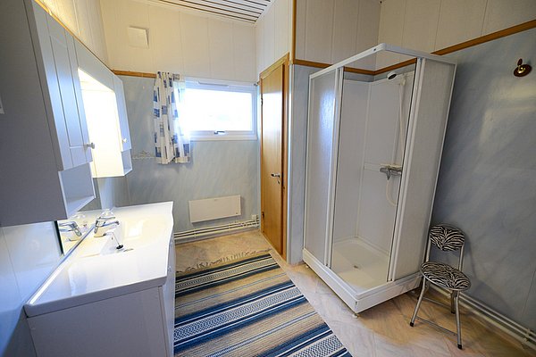 Helles Badezimmer in Nord-Norwegen mit Dusche, Doppelwaschbecken, gestreiftem Teppich und Fenster. Ideal für Angelreisende, die Komfort und Funktionalität nach einem erlebnisreichen Tag am Wasser suchen.