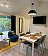 Gemütlicher Wohnbereich in Hitra, Norwegen: Modernes Interieur mit Esstisch, TV und blauem Sessel. Große Fenster bieten Ausblick auf die Natur. Ideal für entspannte Angelurlaube.