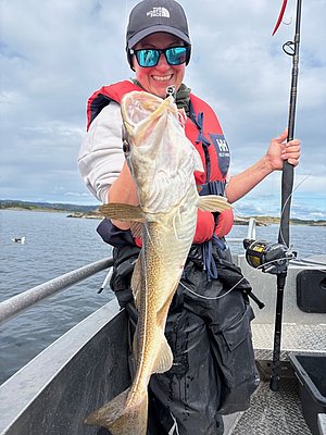 Angler hält frischen Fang auf einem Boot vor der malerischen Küste Hitrias, Norwegen. Perfektes Ziel für Angelreisen mit beeindruckenden Fangchancen. Ideal für Abenteuerlustige und Naturfreunde.