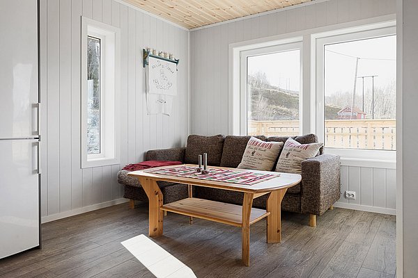 Helles, gemütliches Wohnzimmer in Nordland, Norwegen. Moderne Holzmöbel, große Fenster mit Ausblick auf eine ruhige Landschaft. Ideal für Angelurlauber, die Entspannung suchen. Perfekt als Basis für Abenteuer und komfortables Wohnen.